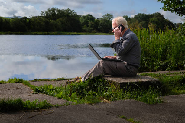 istock Senior man outdoors with a mobile phone and laptop 1418223489