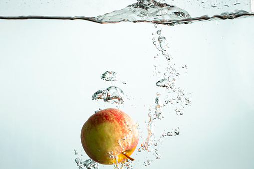 A close-up shot of an apple being dropped into water.