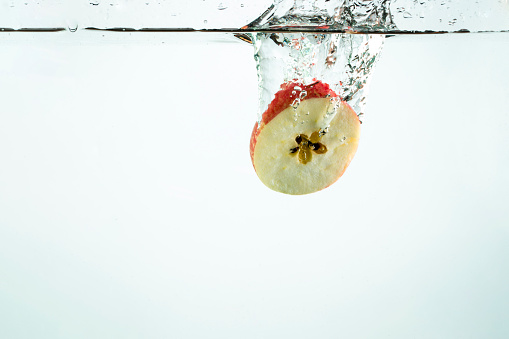 A close-up shot of half an apple being dropped into water.