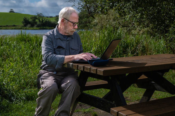 istock Senior man sitting on a picnic bench with a laptop 1418224520