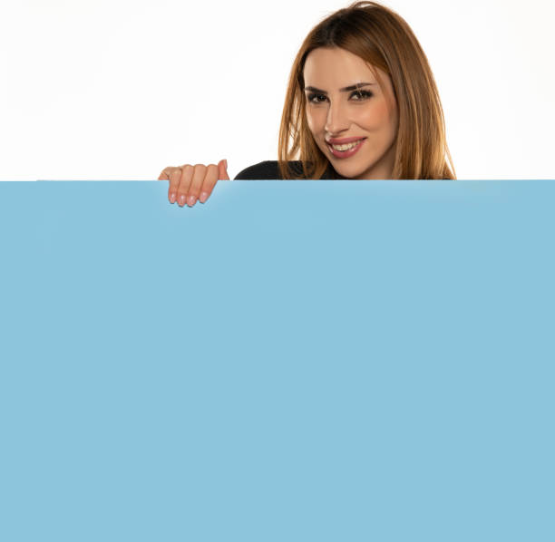 istock a young advertizing excited woman peeks behind a empty blue board 1418225019