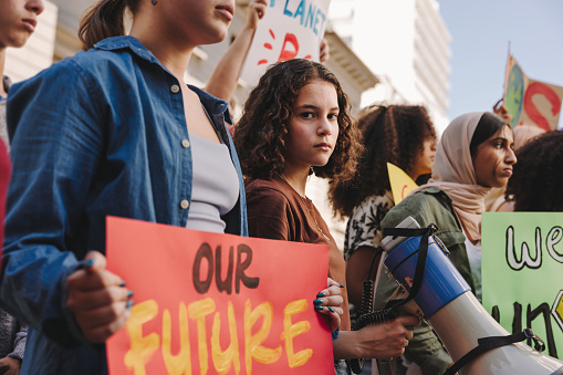 Teenage girl holding a megaphone while marching for climate justice with a group of demonstrators. Multicultural youth activists protesting against global warming and climate change.
