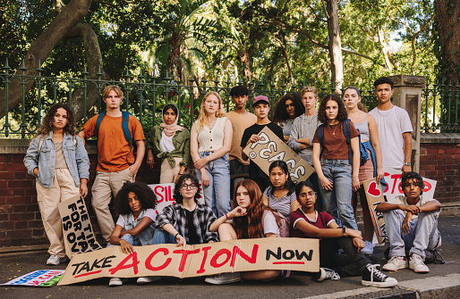 Group of multiethnic youth activists looking at the camera while displaying anti-war posters and banners. Diverse young people holding a peace and human rights demonstration.