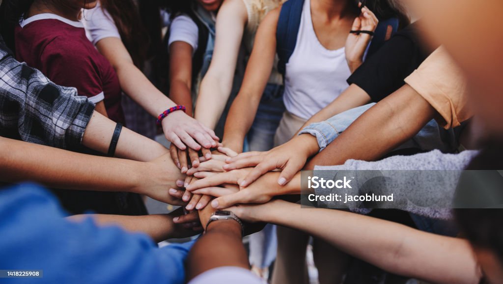 Multicultural teenagers expressing their unity and teamwork Multicultural teenagers putting their hands together in a huddle. Group of unrecognizable young people expressing their unity and teamwork Unity Stock Photo