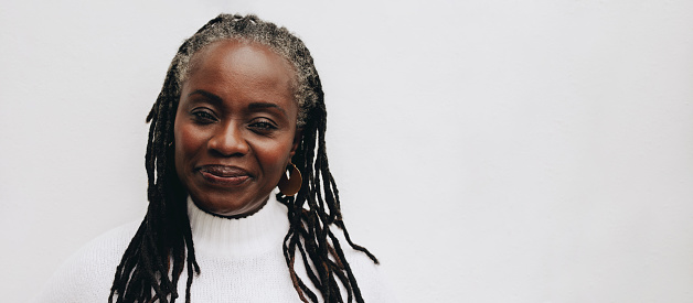 Confident woman with dreadlocks looking at the camera while standing against a white background. Mature black woman embracing her natural hair.