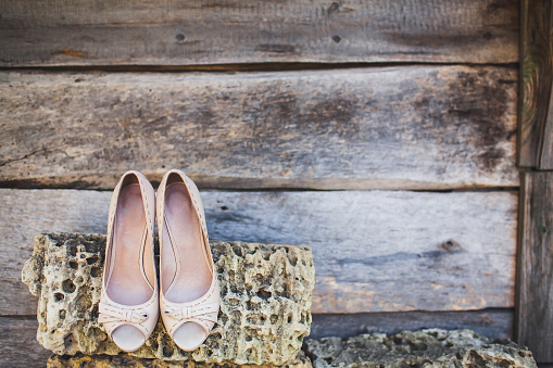 Beige wedding shoes hanging on a stone.