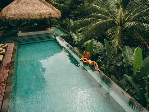 Aerial shot of man and woman relaxing at the poolside. Couple enjoying holiday at luxury resort.