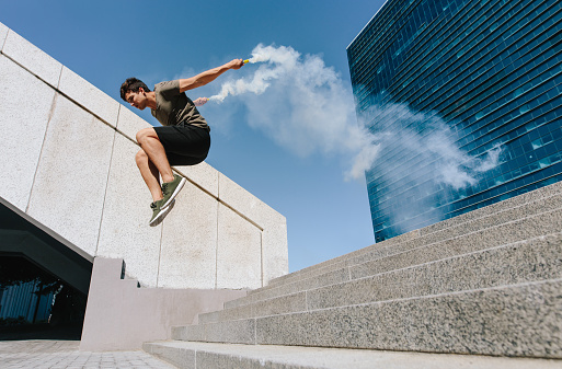 Young man jumping high over stairs outdoors with smoke grenades. Free runner jumping over some steps in urban space.