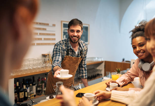istock Handsome bartender serving coffee to customers in cafe and smiling 1418232575
