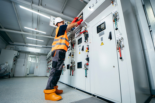 Adult electrician builder engineer testing and screwing equipment in fuse box and repairing of modern electricity power station using voltmeter. Automatic control cabinet