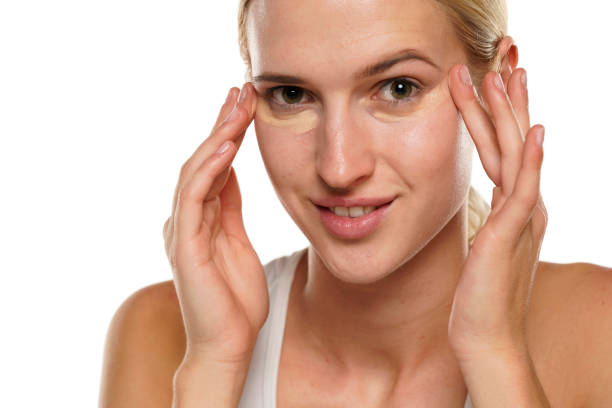 istock Young blond smiling woman applying concealer under her eyes 1418235615