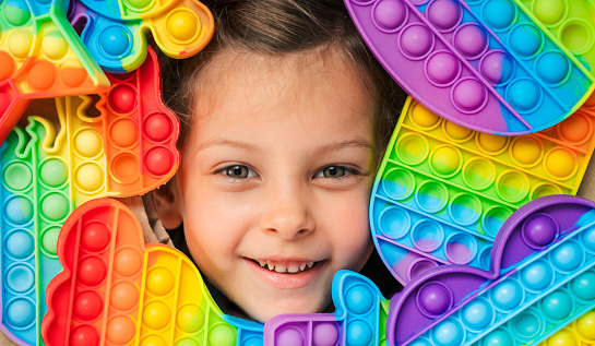 Little girl,kid,child head among many,lots of colorful pop it. Children play. Trendy silicone antistress colorful sensory push toy popit. Flapping fidget. Rainbow color.Cure of autism.Stress reliever.