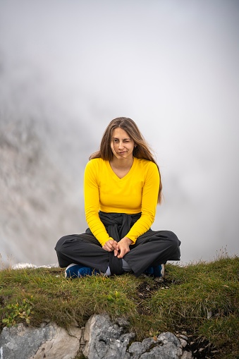 A vertical shot of a young gorl sitting on the top of a mountain against white fog