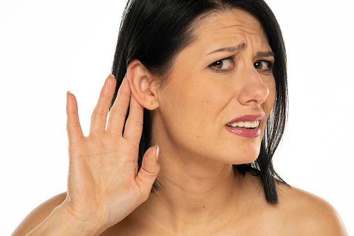 Middle aged woman over isolated white background listening to something by putting hand on the ear