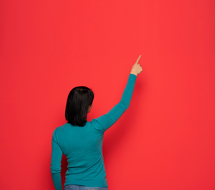 Rear view of a woman pointing at something on a red wall