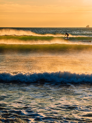 Paddle surfing in ocean at waves. Surfer on sea wave with warm tones of sunset.