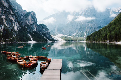 One of the most beautiful Italian lakes Braies at sunset with foggy mountains, forest and boats. Clean turquoise water view with reflections, lakeside in Dolomites region with mountain pass around all lake.