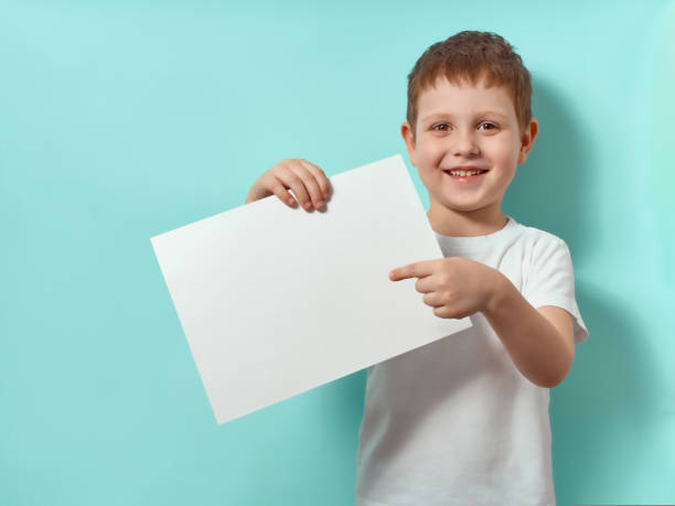istock Little boy holds blank paper sheet, blue background 1418245339