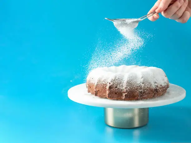 Photo of Female hand sprinkling icing sugar on bundt cake