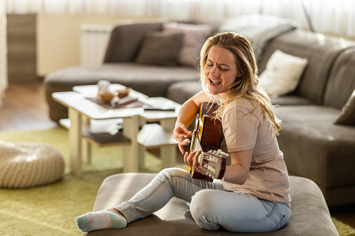 Happy woman playing acoustic guitar in living room