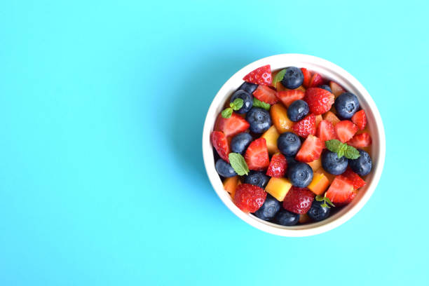 istock Fruit salad in a white cup on a soft blue background. Sliced strawberries, peaches and blueberries with mint leaves. Free space for text. 1418253544