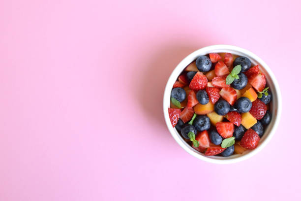istock Fruit salad in a white cup on a pink background. Sliced strawberries, peaches and blueberries with mint leaves. Free space for text. 1418253784