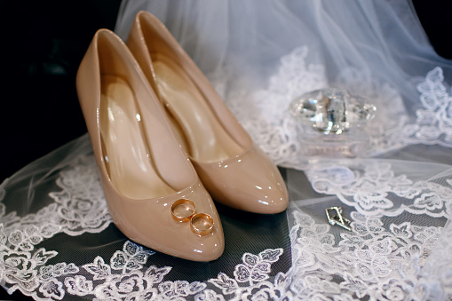 The bride's wedding shoes with wedding rings. Gathering the bride in the morning and preparing for the wedding day. Top view of gold wedding rings, perfume and earrings on lace veil
