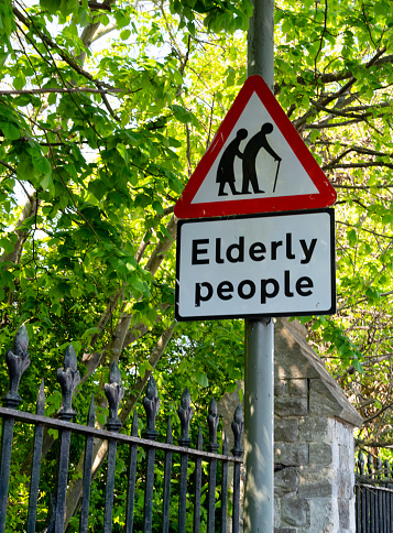 Outside an urban cemetery fence, a sign warning of ‘Elderly People’. (A care home is nearby.)