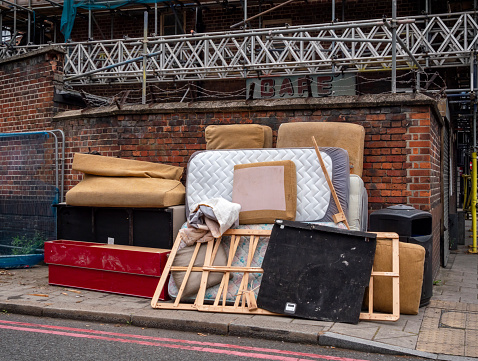 A pile of fly-tipped furniture on the corner of a street in Southwark, South East London. Neatly stacked, it includes a mattress - with fitted sheet - a sofa, bed base, wood and some fabric.