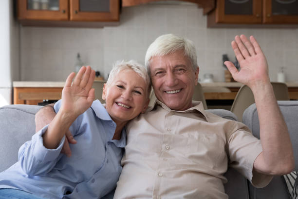 istock Older couple sit on sofa looking at camera start videocall 1418260572
