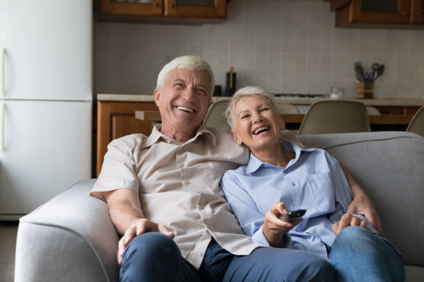 istock Older couple relax on sofa laughing switch channels enjoy movie 1418260609