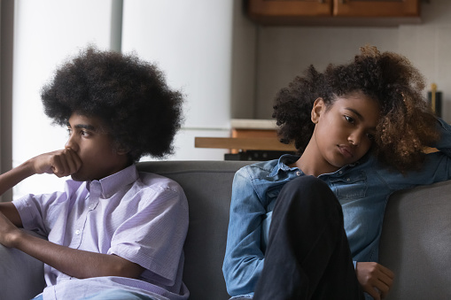 Sad silent African teenagers couple after fight sit apart on sofa, avoid talk, think about break up, troubles in relations, having problems in relationships, first love, quarrels, heartbreak concept