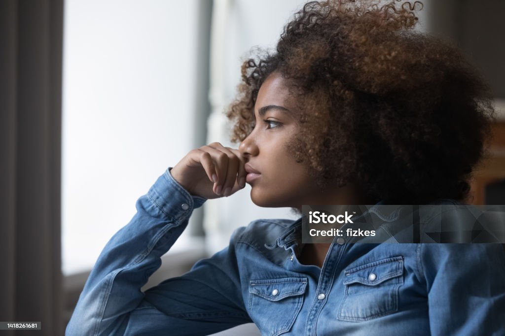 Closeup face African sad thoughtful teenager girl looking into distance Close up side profile view face of African sad thoughtful teenager girl sit on sofa at home looking into distance feels unhappy, first unrequited love, teen relation problem, break up, worries concept Anxiety Stock Photo