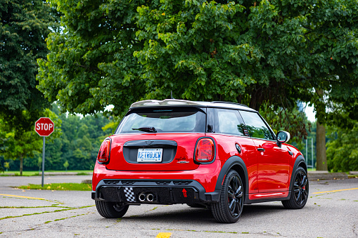 Toronto, Ontario, Canada- August 26, 2022. Chili red colour MINI COOPER on the road in public park in Toronto East side, Canada. This is the third generation model F56 JCW, since BMW took over iconic brand of MINI. MINI featured in the photo is John Cooper Works model, the most powerful 2 door version. For the first time, this compact car features engine build and designed by BMW, and packs even more power and torque than previous models since 2002 to present. Original design clues and themes are still present on this brand new model. Mini has been around since 1959 and has been owned and issued by various car manufacturers.