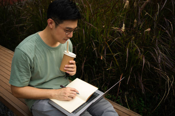 Mature adult man Programmer Student learning online class with Virtual Tutor on laptop computer at park
