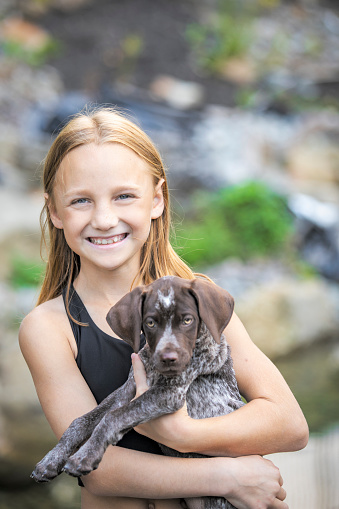 A happy ten year old girl holding her German Shorthair Pointer puppy outdoors.