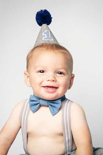 A one year old baby boy in his party hat posing for a picture.