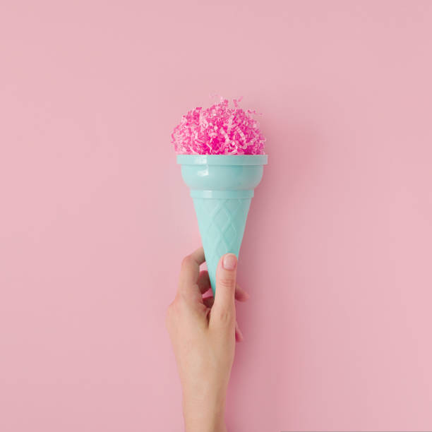 Woman hand hold pink paper ice cream scoop with ice cream plastic cone on pastel pink background. Minimal summer concept. Micro plastic in food. Recycling. stock photo
