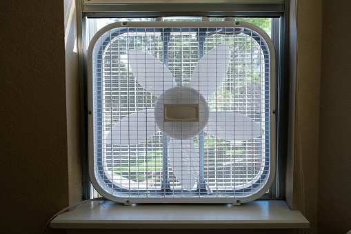 Classic window box fan inserted in home room window indoor cooling air conditioning vetilation equipment. front view hight quality close up photo.