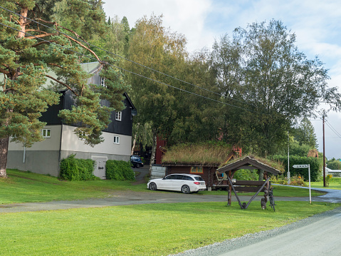 Storen, Norway, September 7, 2019: View of Classical Norwegian Camping site with traditional wooden cabin with turf grass roof, lush green grass and trees. White car parked in front of cottage, Central Norway.