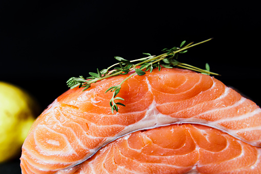 Fresh raw salmon fillet with seasonings and herbs, close-up on black background.