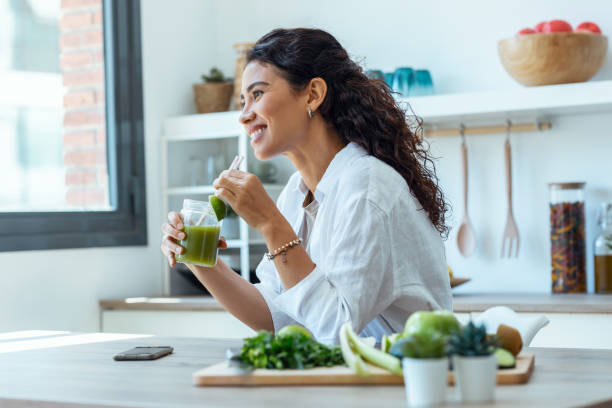 симпатичная женщина смотрит в сторону, пока пьет фруктовый детокс-сок на кухне дома. - smart casual occupation casual healthy eating стоковые фото и изображения