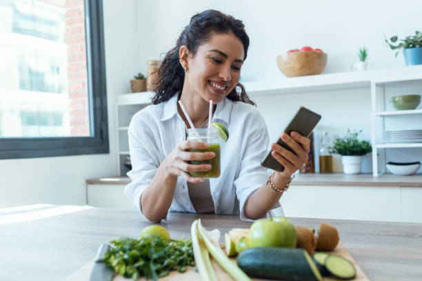 istock Pretty woman using her mobile phone while drinking fruit detox juice in the kitchen at home. 1418282825