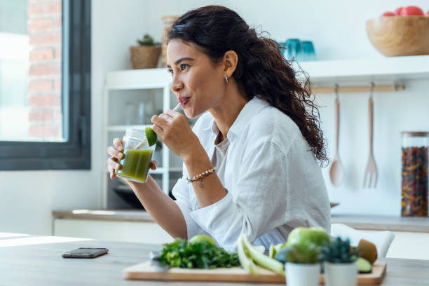 mujer bonita que busca de lado mientras bebe jugo de desintoxicación de frutas en la cocina de casa. - healthy eating fotografías e imágenes de stock