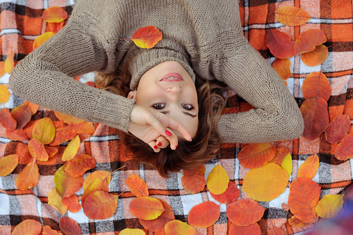 Woman relaxing on the plaid with fallen autumn leafs