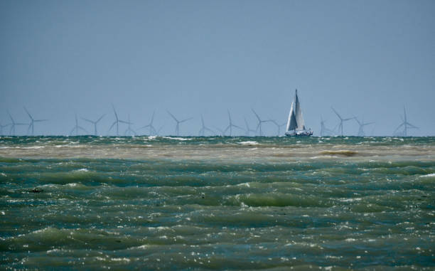 Yacht sailing past Rampion Wind Farm near Cuckmere Haven, East Sussex, England