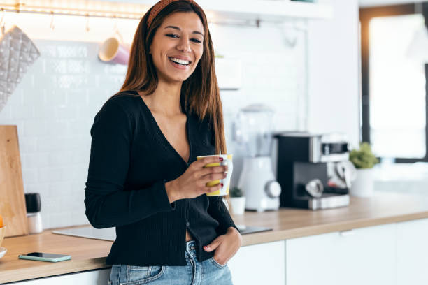 istock Beautiful young woman drinking coffee while standing in the kitchen at morning 1418289441