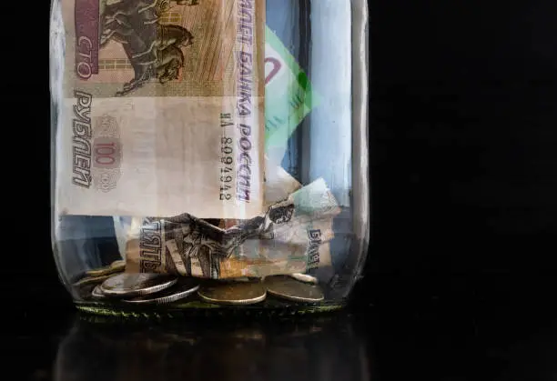 Photo of Crumpled paper banknotes of Russian rubles and metal coins inside a glass jar