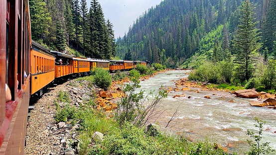 San Juan County, Colorado, USA - July 12, 2021: View of the Animas River and the Durango & Silverton Narrow Gauge Railroad train as seen from a passenger’s perspective out the window of a train car.