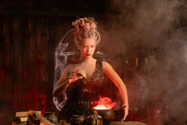 Halloween Witch with cauldron. Beautiful young woman conjuring, making witchcraft. Standing spooky dark magic dungeon dark room. Enchantress prepare love potion use magiÑ spell